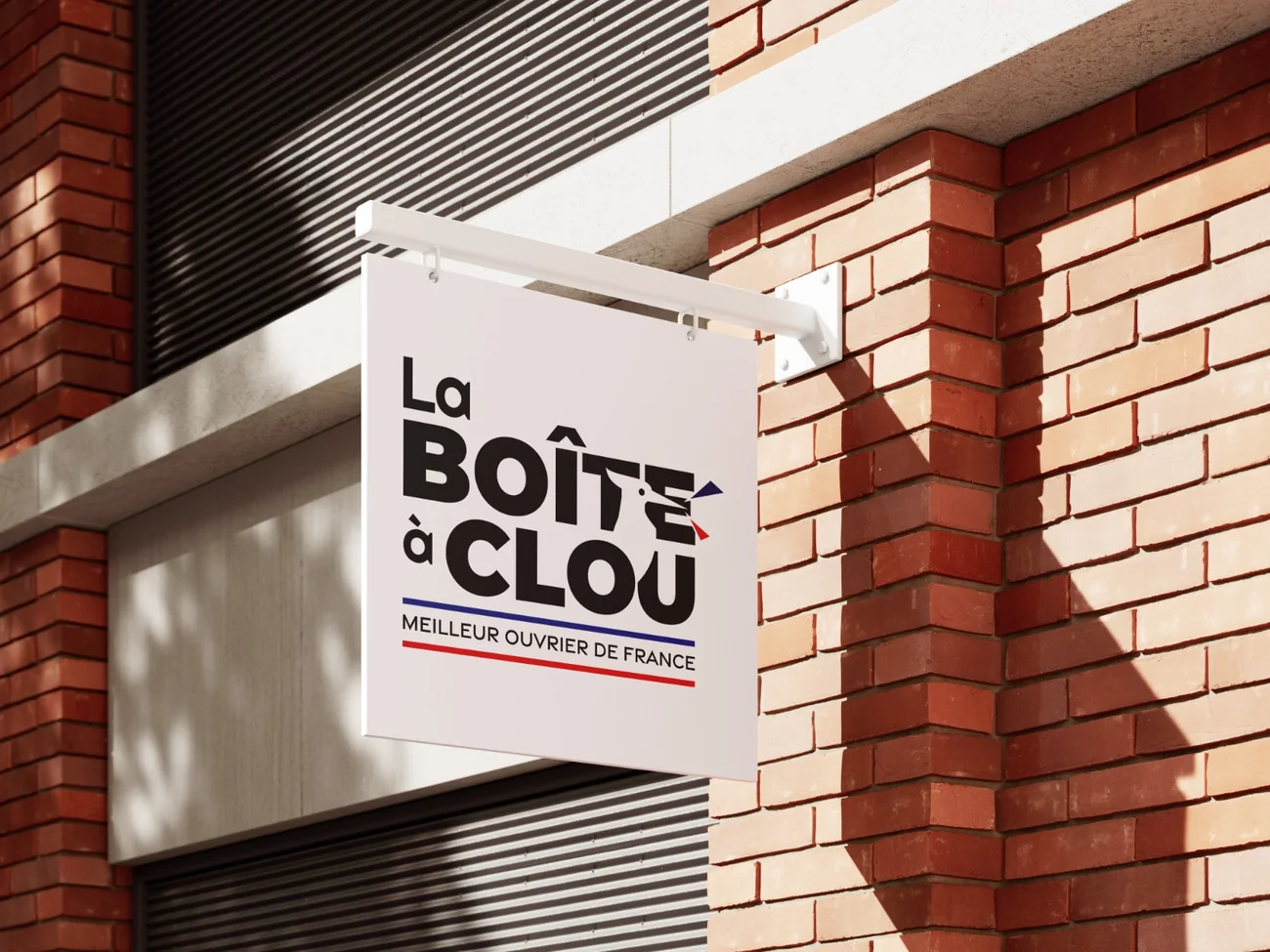 Enseigne drapeau La Boîte à Clou fixée sur une façade en brique